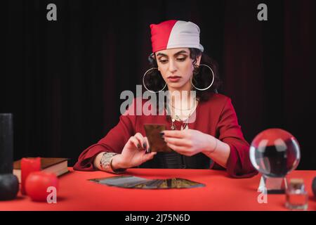 Gypsy fortune Teller regardant la carte de tarot flou près de verre orbe sur la table isolée sur noir Banque D'Images