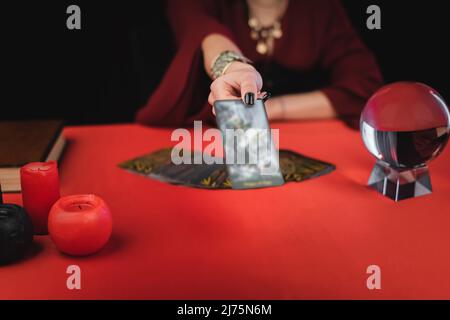 Vue rognée d'un support flou montrant une carte de tarot près des bougies et de l'orbe isolée sur le noir Banque D'Images