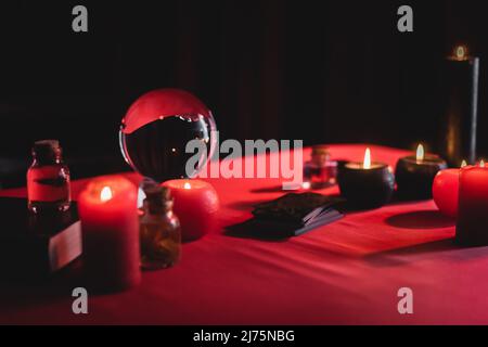 Bougies brulantes près de l'orbe magique et des cartes de tarot isolées sur le noir Banque D'Images