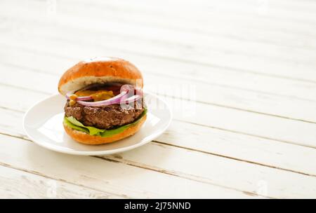 Un hamburger sur une plaque blanche sur une table de pique-nique blanche Banque D'Images