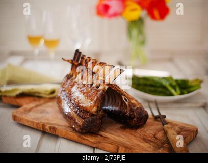 Carré d'agneau sur une planche à découper avec asperges et vin en arrière-plan Banque D'Images