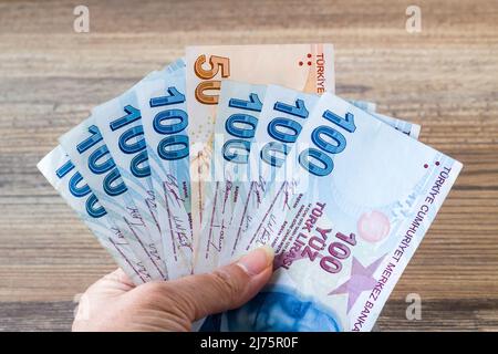 Une main tenant cent cinquante billets turcs sur une surface en bois Banque D'Images