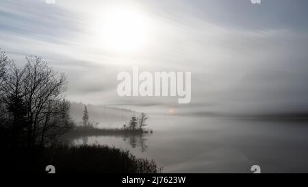 La petite chapelle Maria Rast près de Krün brille comme une lueur d'espoir à travers le brouillard au-dessus du petit lac de la lande dans les Alpes bavaroises. En arrière-plan les montagnes Karwendel l'ombre, tandis que le paysage est illuminé par la pleine lune, qui n'est pas visible, au premier plan un petit promontoire dans le Waser, avec des arbres et des buissons. Banque D'Images