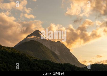 Lumière du soir avec une atmosphère spéciale de nuages sur le Wetterstein au-dessus de Mittenwald. Dans certaines images de cette série encore un aigle doré vole en petit près de la croix de sommet Banque D'Images