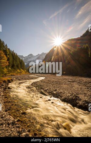 Soleil du soir en automne à Johannisbach à Johannistal près de Hinterriss à Karwendel, Tyrol / Autriche. Le ruisseau de montagne serpente à travers son lit de gravier naturel tandis que le soleil se couche sur la pente de montagne, en arrière-plan les murs de Laliderer avec de la neige. Banque D'Images