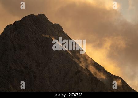 Lumière du soir avec une atmosphère spéciale de nuages sur le Wetterstein au-dessus de Mittenwald. Dans certaines images de cette série encore un aigle doré vole en petit près de la croix de sommet Banque D'Images