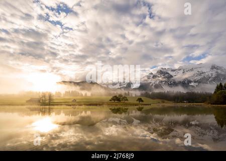 Ambiance matinale au lever du soleil à Schmalensee, dans les contreforts bavarois des Alpes, près de Mittenwald. En arrière-plan le Karwendel et une petite péninsule avec quelques arbres. Les nuages et le brouillard encadrissent l'ambiance. Banque D'Images