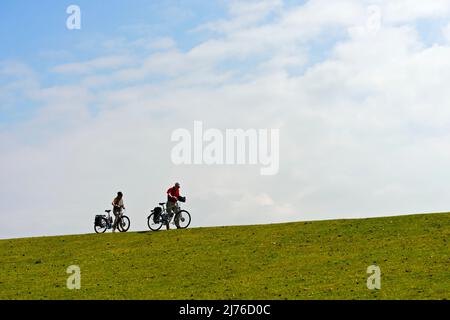 Deux cyclistes poussant leurs vélos sur un sommet de digue, Parc national de la mer des Wadden du Schleswig-Holstein, Westerhever, Schleswig-Holstein, Allemagne Banque D'Images