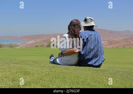 Un couple aimant assis dans l'herbe, relaxant tout en regardant le paysage. Banque D'Images