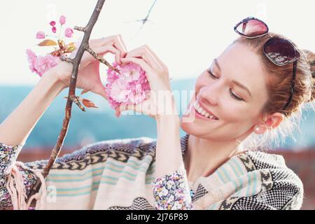 Jeune femme formant le cœur avec fleur de cerisier en plein air Banque D'Images