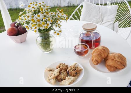Vue de dessus des croissants frais sucrés sur la table avec thé et un vase de pâquerettes. Petit déjeuner le dimanche dans l'arrière-cour du cottage. Photo de haute qualité Banque D'Images
