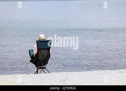 Homme assis dans la chaise pliante sur la plage, reposant près du lac. Vue de l'arrière Banque D'Images