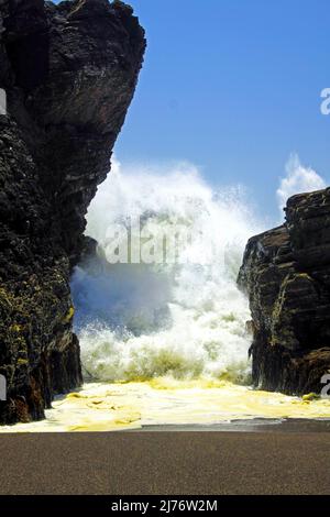 Crique isolée de plage de sable noir de lave, puissantes vagues violentes de surf se brisant entre les rochers, mousse vaporisée de mer brumeux - Cobquecura, Chili, Pacifique Banque D'Images