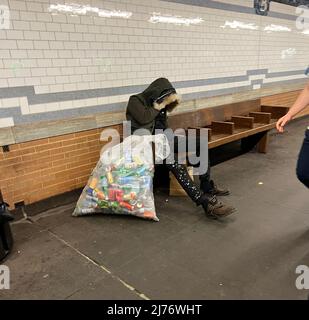 L'homme dort sur un banc sur une plate-forme de métro à Manhattan avec un sac plein de boîtes en aluminium qu'il est rassemblé pour gratter quelques dollars. Manhattan, New York. Banque D'Images