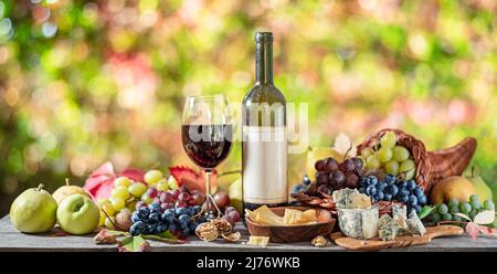 Raisins, bouteille de vin et différents fromages sur table en bois de campagne et flou coloré automne fond. Variété de produits comme symbole de l'autu Banque D'Images