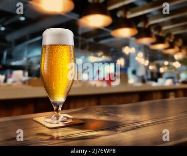 Verre de bière refroidi avec condensation sur la table en bois. Barre floue à l'arrière-plan. Banque D'Images
