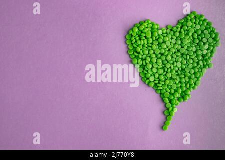 De beaux granules de cire verte avec de l'extrait d'Aloe pour l'épilation sont versés sur un fond violet clair, en forme de coeur. Épilation, épilation, Banque D'Images