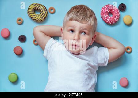 Mignon enfant souriant sur des beignets et des macarons français sur fond bleu. Concept de la Journée nationale du Donut. Concept d'enfance heureuse. T-shirt blanc maquette. Banque D'Images