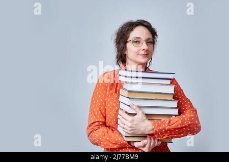 Une femme d'âge moyen tient une pile de livres de fond. Banque D'Images
