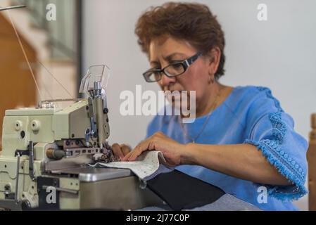Couturière latine mature à l'aide d'une machine à coudre des pièces de tissu Banque D'Images