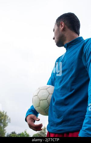 Homme tenant une balle de football blanche dans une journée nuageux au parc Banque D'Images