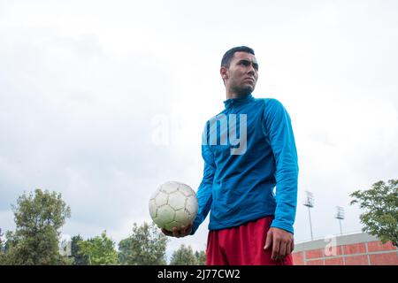 Homme tenant une balle de football blanche dans une journée nuageux au parc Banque D'Images