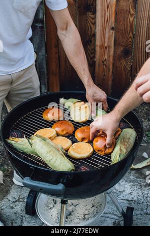 deux gars qui grillent des petits pains à hamburger et du maïs en rafle en été Banque D'Images