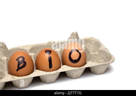Gros plan de trois œufs bruns dans une boîte en carton gris recyclé non coloré avec le mot bio signifie bio sur un fond blanc comme un concept pour Banque D'Images