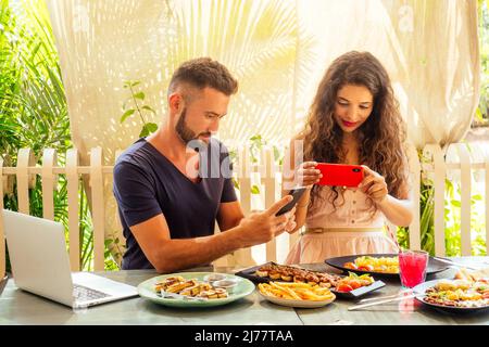 belle femme indienne et homme arabe photographiant des plats dans un café tropical d'été sur l'appareil photo Banque D'Images