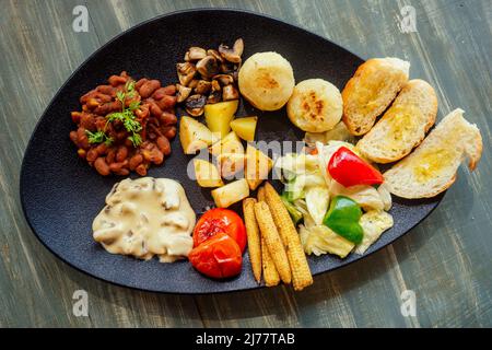 délicieux haricots rouges sur le pain avec pomme de terre et tomate, épis de maïs frits avec champignons sur plat noir repas bio végétalien Banque D'Images