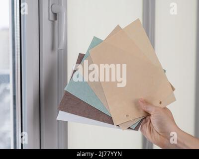 Femme tenant des échantillons de tissu de stores roulants contre le fond de fenêtre. Banque D'Images