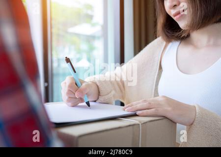 Gros plan l'homme de livraison dans un emballage de maintien d'uniforme rouge tandis que la femme cliente signe la signature sur le papier des documents de réception. Banque D'Images