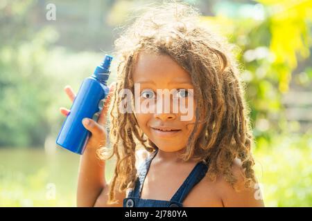 Mowgli garçon indien avec des dreadlocks cheveux se cachant tenant moustique spray dans les tropiques vert forêt fond Banque D'Images