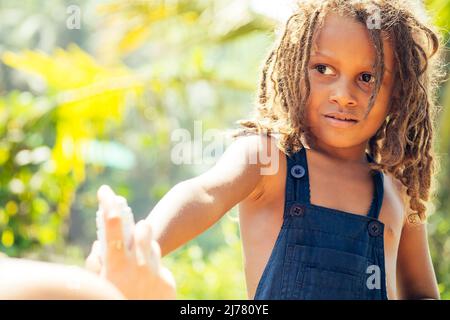 Mowgli garçon indien avec des dreadlocks cheveux se cachant tenant moustique spray dans les tropiques vert forêt fond Banque D'Images