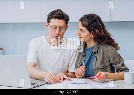 Le couple est assis dans la cuisine boissons café pour le petit-déjeuner et parle de dessins de rénovation d'appartement faire des notes dans l'ordinateur portable et le bloc-notes Banque D'Images