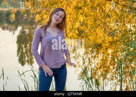 Jeune femme gaie en jeans sur la rive du lac avec feuillage automnal Banque D'Images