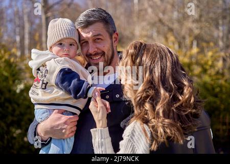 Une famille avec un petit bébé. Père tenant sa fille sur les mains. Écoute de bébé à l'appareil photo. Mère tenant la main de l'enfant. Banque D'Images