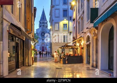 Scène de rue le long de la rue de la Madelaine dans la vieille ville de Nîmes, en France avec l'église Saint-Paul en arrière-plan. Banque D'Images