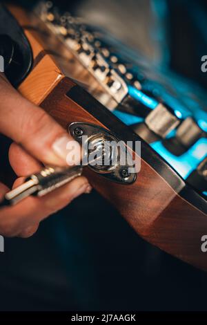 Gros plan des doigts mâles reliant le câble à la prise d'entrée d'une guitare basse électrique Banque D'Images