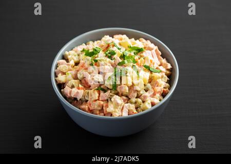 Salade Olivier maison dans un bol sur une surface en bois noir, vue latérale. Banque D'Images