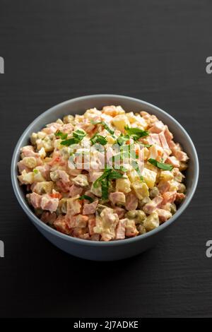 Salade Olivier maison dans un bol sur fond de bois noir, vue latérale. Banque D'Images