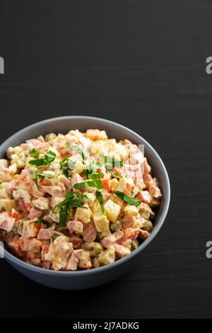 Salade Olivier maison dans un bol sur fond de bois noir, vue en angle bas. Banque D'Images