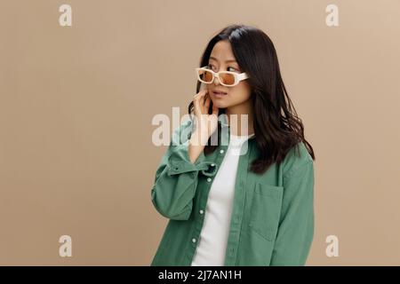 Happy Averyeplaisir la jeune femme coréenne en kaki vert chemise lunettes stylées a l'air de poser isolé sur un fond beige pastel studio. Mode tendance Banque D'Images