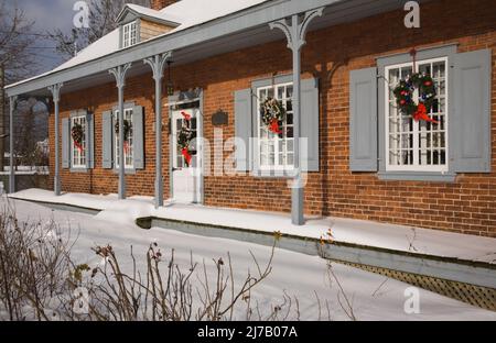 Ancienne maison en briques nuancées rouges de style Canadiana 1800s avec couronnes de Noël sur la façade en hiver. Banque D'Images