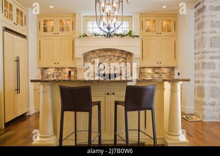 Île élégamment conçue avec des chaises bistro en cuir marron à haut dossier dans la cuisine à l'intérieur d'une maison luxueuse. Banque D'Images