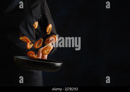 Des crevettes géantes dans une poêle en vol gelé sur fond noir. Le processus de cuisson des fruits de mer par un chef professionnel. Recettes pour le restaurant et la maison Banque D'Images