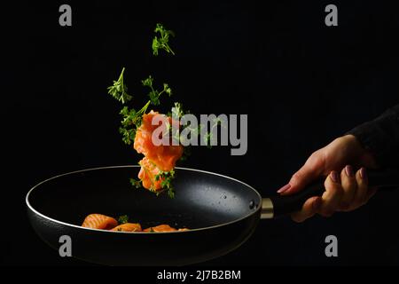 Morceaux de poisson rouge avec persil dans une casserole dans un vol gelé sur fond noir. Prise de vue macro. Restaurant, hôtel, banquet, pique-nique. Publicité, bannière Banque D'Images