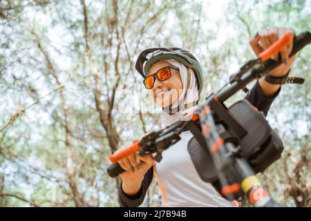 jolie fille voilée dans des lunettes de soleil souriant tout en faisant du vélo dans le parc Banque D'Images