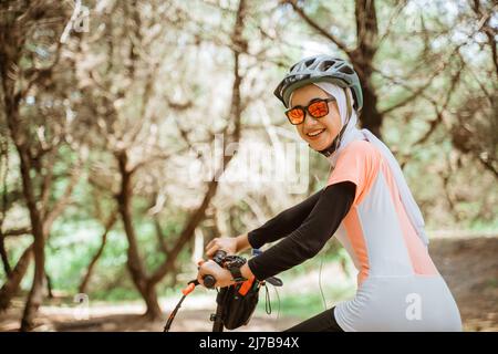 fille voilée dans des lunettes de soleil souriant portant des écouteurs à vélo dans le parc Banque D'Images