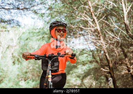 femme asiatique en lunettes de soleil vélo dans le parc avec des arbres de fond Banque D'Images